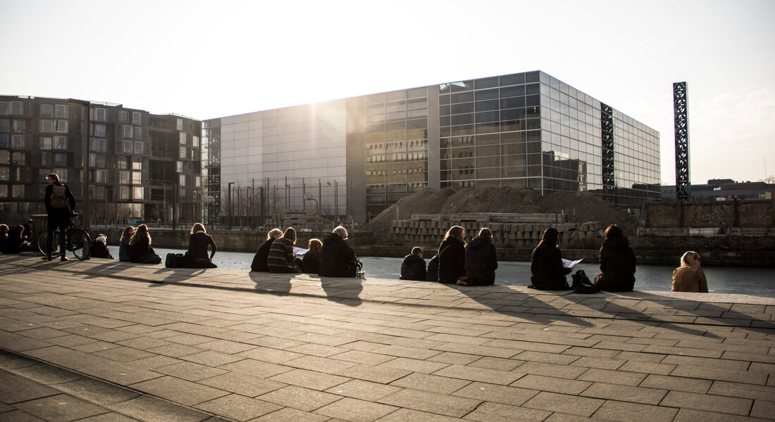 KU studerende sidder foran kanalen i solnedgang med Tietgenkollegiet i baggrunden